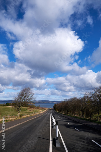 Empty street in Scotland during lockdown. Landscape with white marks to devide the vehicle and the bicycle sides. Horizon with clouds and sea.