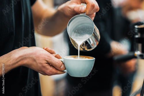Barista hands pouring warm milk in coffee cup for making latte art. Professional coffee making, service