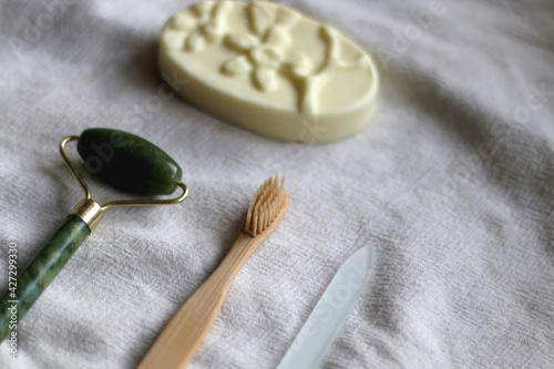 Jade face roller, wooden toothbrush, glass nail file and bar of soap. Sustainable body care products. Selective focus.