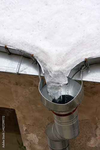 Melting ice and snow on the roof at the drainpipe