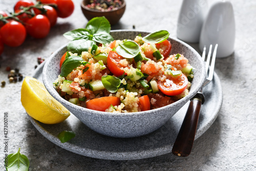 Light salad with tomatoes, cucumber and quinoa with olive oil and basil on a concrete background.