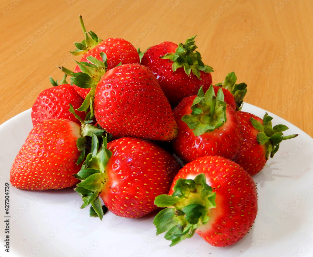 Pile of strawberries on a white plate on a wooden table. No people. Pile of strawberries on a white plate on a wooden table. No people.