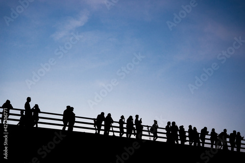 Gente a contraluz parada sobre un puente. 