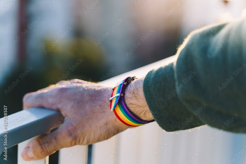 close-up view of a man's hand with an LGBT rainbow wristband.