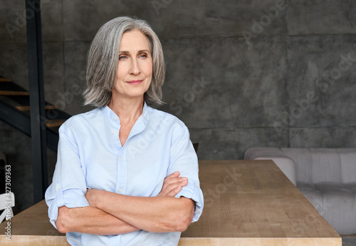 Bilde på lerret Thoughtful mature 60s old woman standing arms crossed in home office