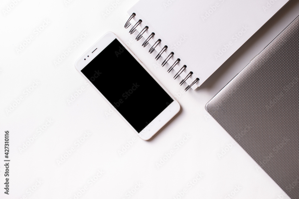 Close laptop on a white background next to a mobile phone and a ring notebook. Close laptop on a white background next to a mobile phone and a ring notebook.