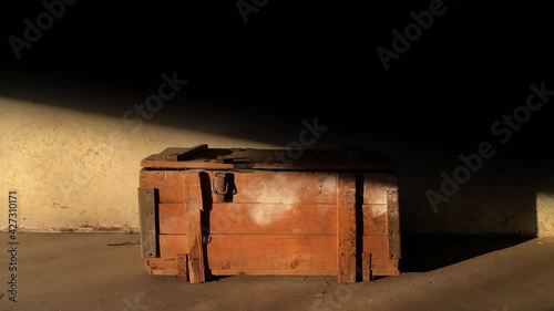 Vertical garage door gate opens to shed light on an old wooden chest against the backdrop of a dirty wall. Treasure hunt