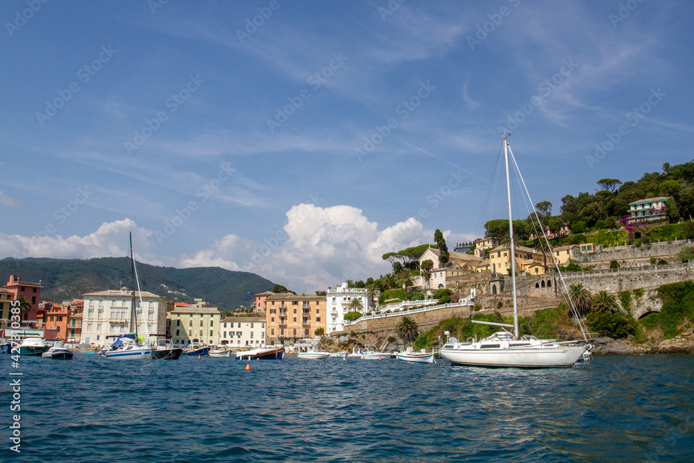 Seascape with azure water in the foreground and Italian port city and rocky coastline in the background