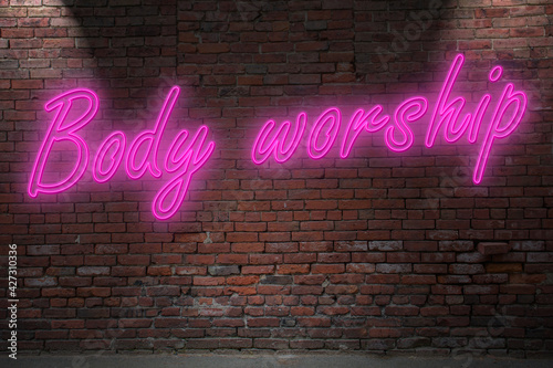 Neon Body worship lettering on Brick Wall at night