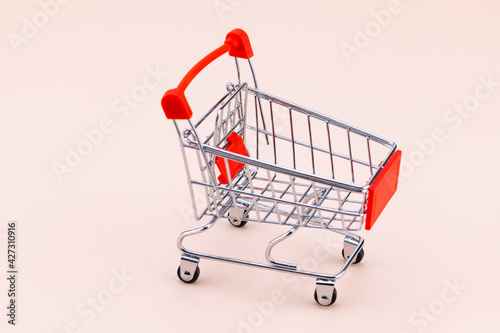 Shopping cart on beige background. Top view with copy space. Shop trolley at supermarket. Sale, discount, shopaholism concept. Consumer society trend