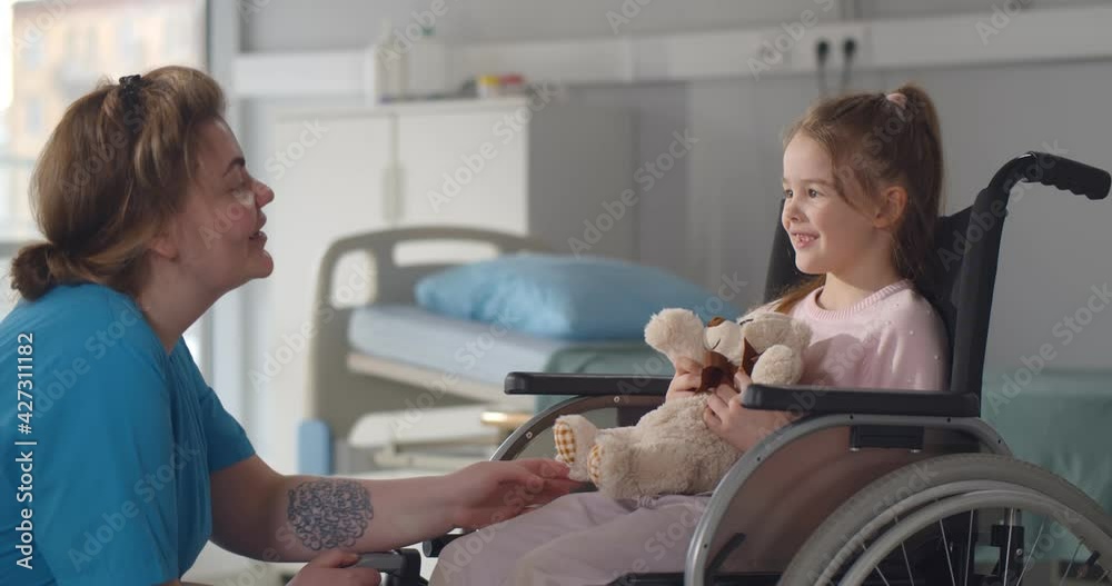 Child patient in wheelchair sitting in hospital ward talking to female nurse Child patient in wheelchair sitting in hospital ward talking to female nurse