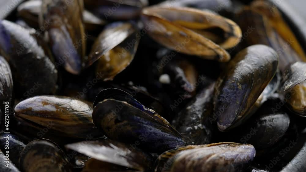 Close up shot of fresh and raw sea mussels in black ceramic bowl placed on dark Close up shot of fresh and raw sea mussels in black ceramic bowl placed on dark