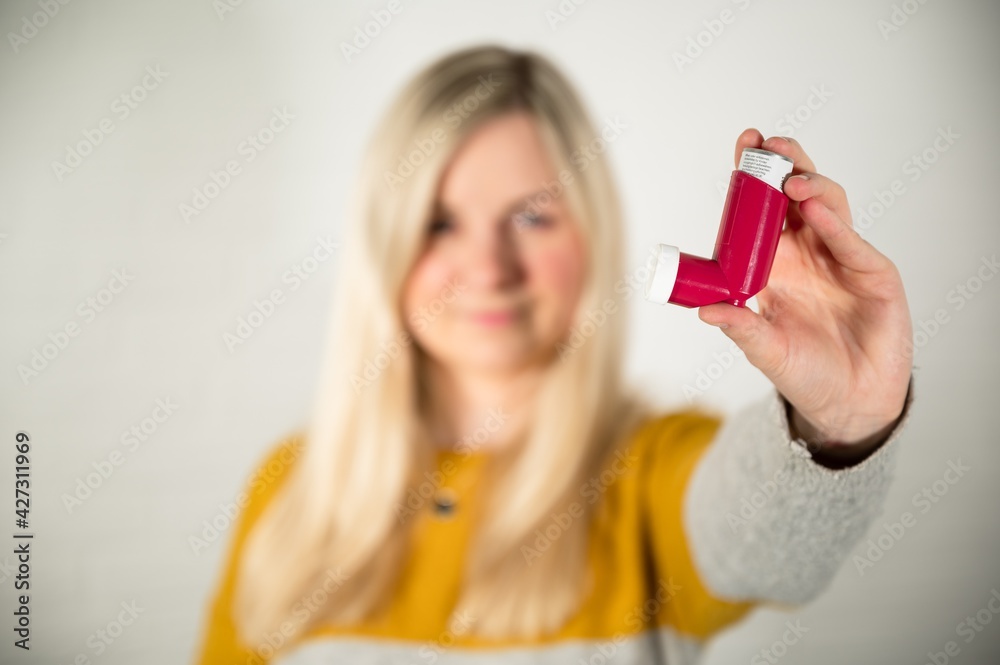 Young blonde woman holding a red asthma spray inhaler in her hand Young blonde woman holding a red asthma spray inhaler in her hand