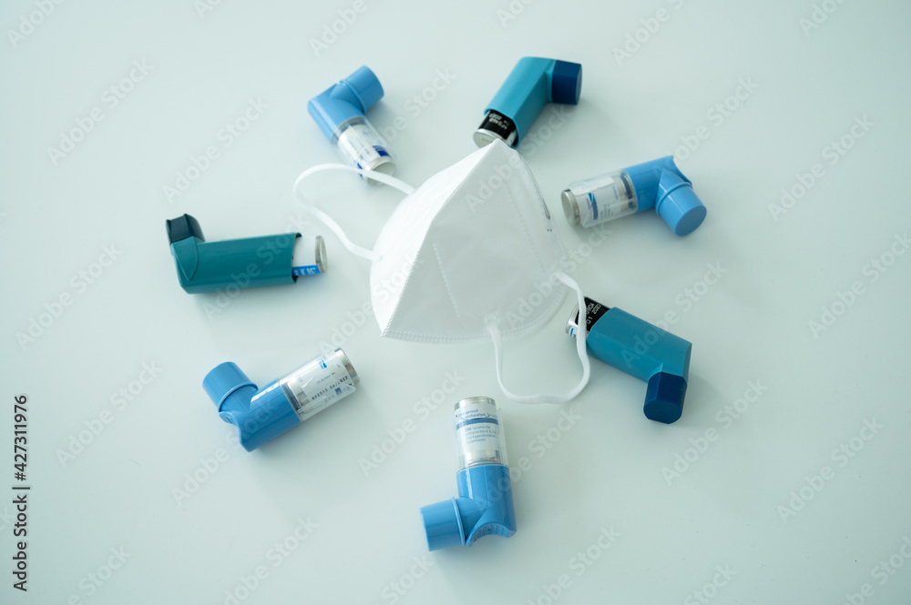 Various asthma spray inhalers and a Covid-19 respirator mask on a white surface