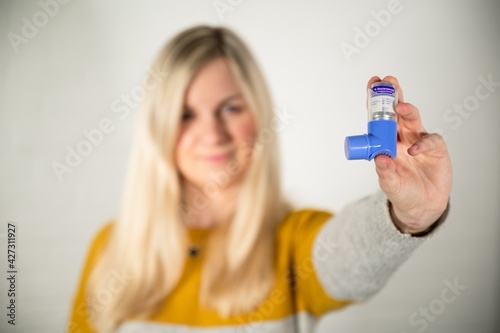 Young blonde woman holding a blue asthma spray inhaler in her hand