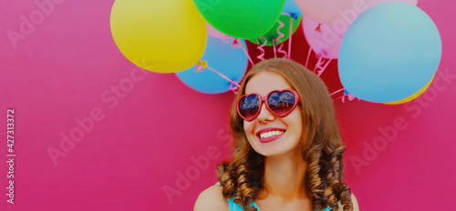 Portrait of happy smiling young woman with colorful balloons looking away on a pink background