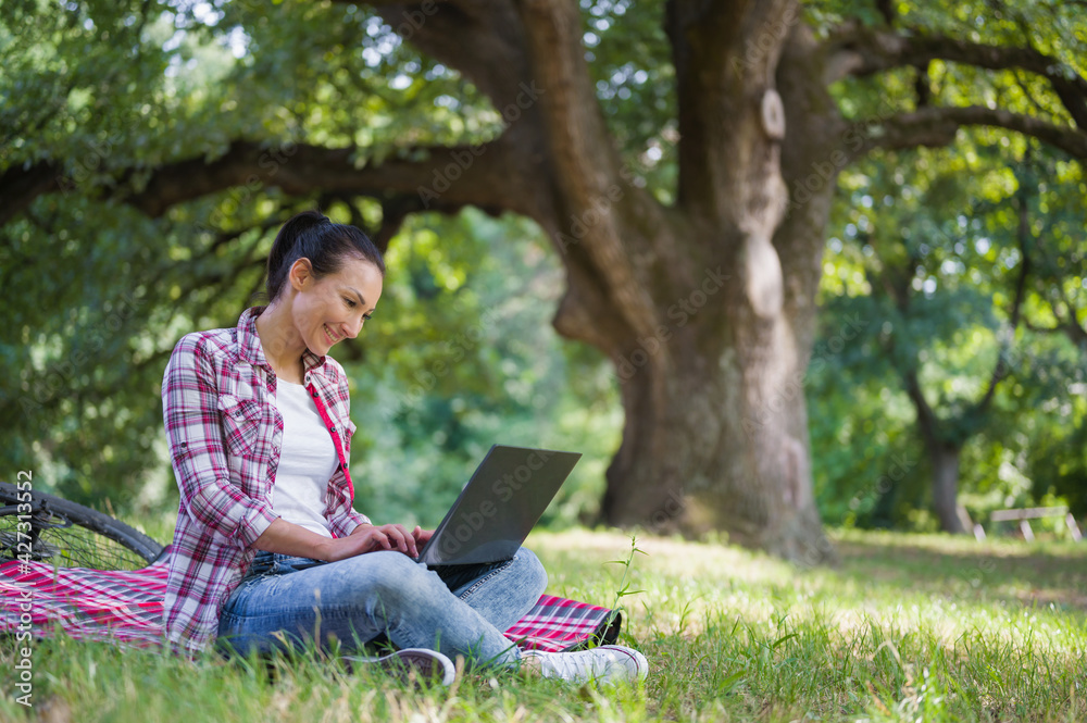 Woman working on laptop computer sitting on a grass in a public park Woman working on laptop computer sitting on a grass in a public park