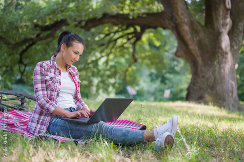 Woman working on laptop computer sitting on a grass in a public park