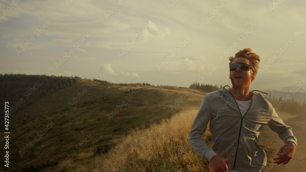 Tired jogger running in mountain landscape. Smiling guy raising hands outdoor