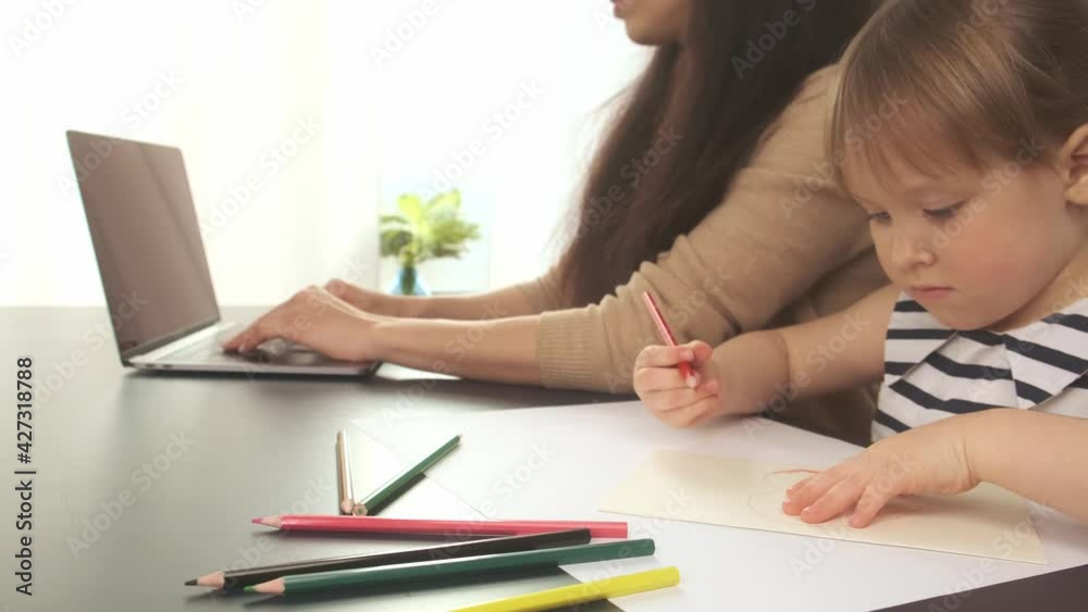 Close-up four year old daughter draws with pencils while her mother works using laptop in home office. Remote work. Pandemic and self-isolation concept Close-up four year old daughter draws with pencils while her mother works using laptop in home office. Remote work. Pandemic and self-isolation concept