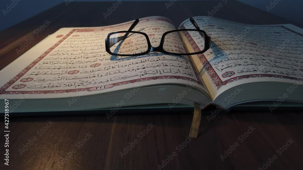 A backward moving shot showing a Quran lying on a table with reading glasses lying on it
