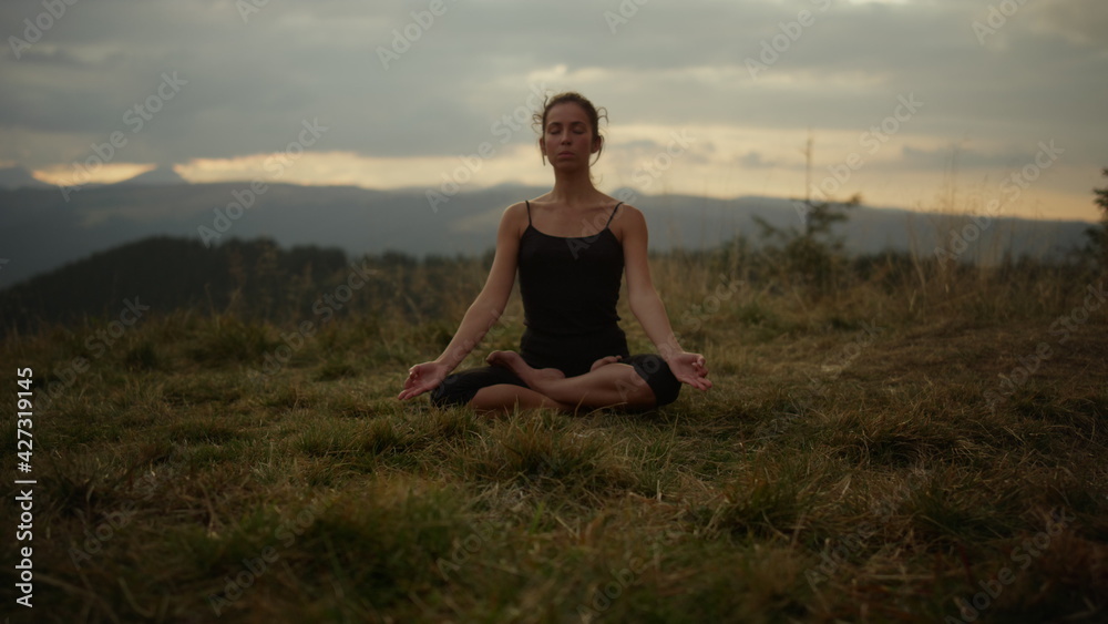 Serious woman sitting in lotus pose on grass. Focused girl meditating outdoor