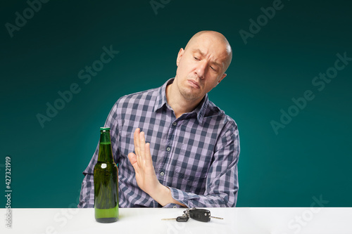Man refusing alcohol beer showing car key as gesture of don't drink and drive isolated over green background.Do not drink alcohol and drive.