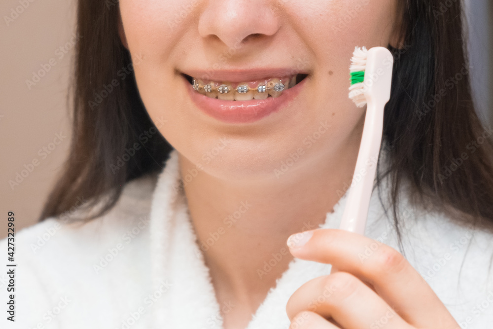 A woman with braces or bracket brushing her teeth with a pink toothbrush in the bathroom. Dental care. Aligning and straightening of teeth. A woman with braces or bracket brushing her teeth with a pink toothbrush in the bathroom. Dental care. Aligning and straightening of teeth.
