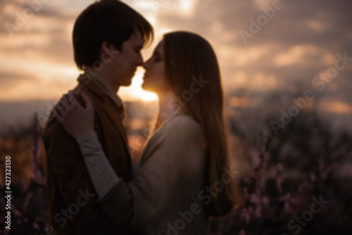 Silhouette of a happy couple in love at sunset in blooming peach rose gardens. Man stands in front of young woman, hugs, kisses with tenderness and passion. Close-up portrait of lovers. Romantic date