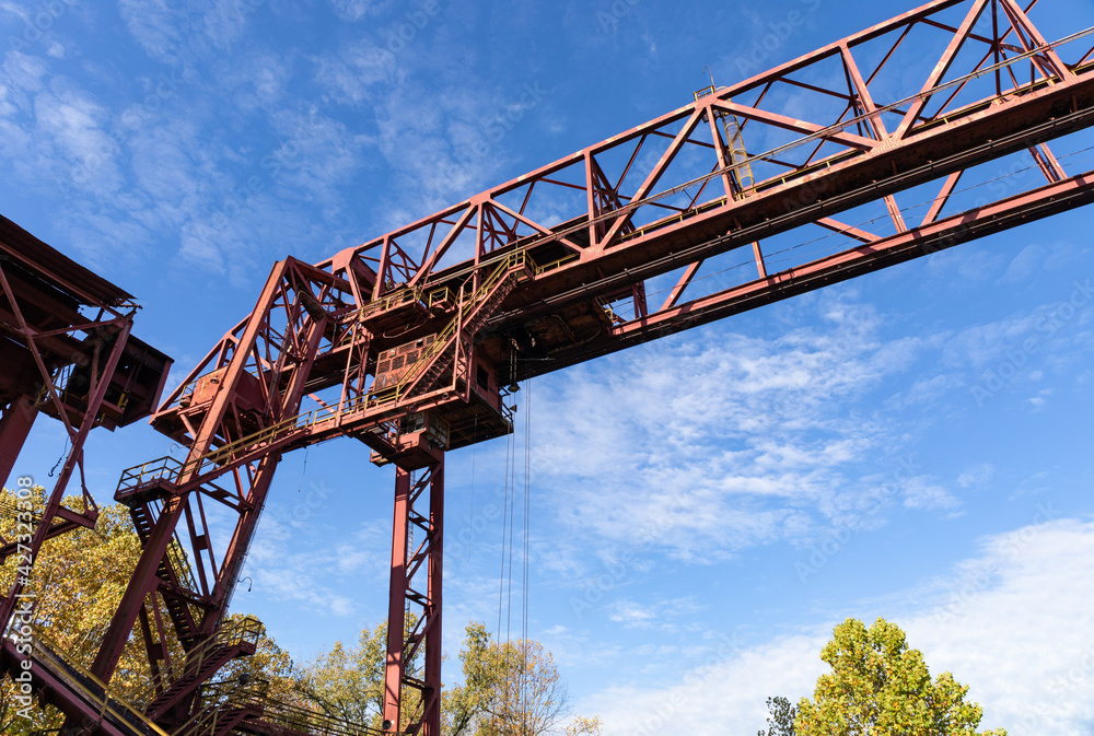 Massive overhead steel structure silhouetted against a bright blue sky, light clouds, horizontal aspect