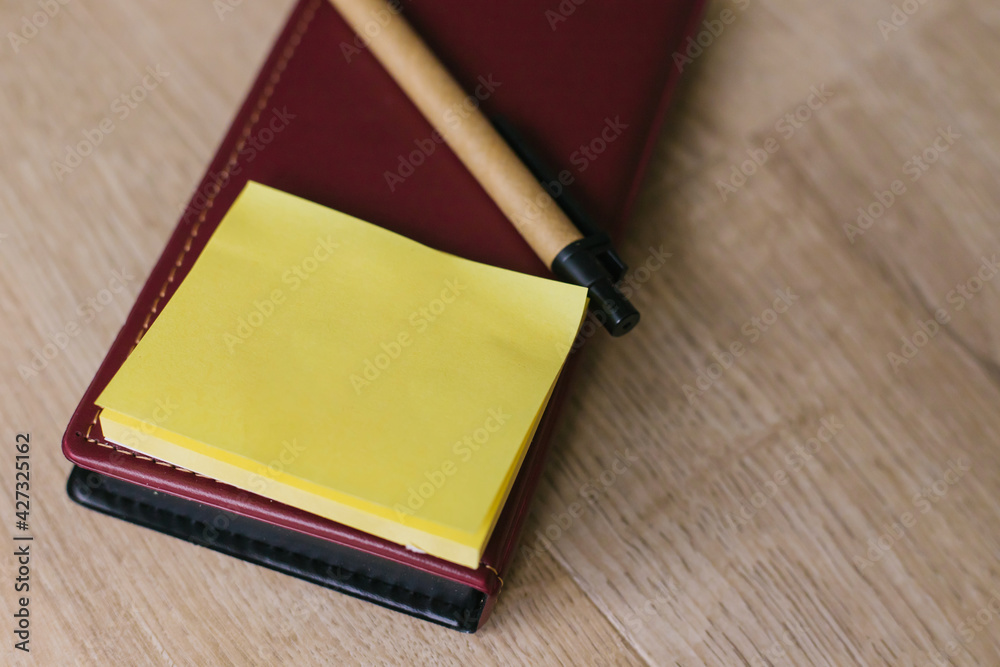 Fototapeta premium Leather notebook with yellow leaves. A paper pen lies next to it on a light wooden background.