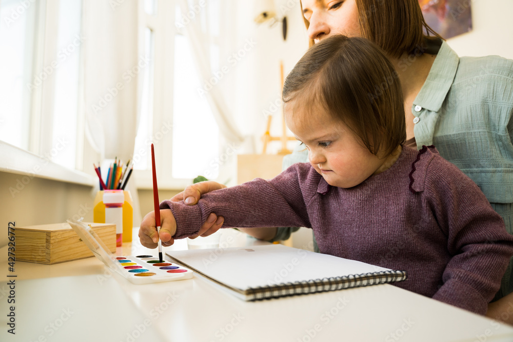Child with down syndrome holding brush and painting on the paper Child with down syndrome holding brush and painting on the paper