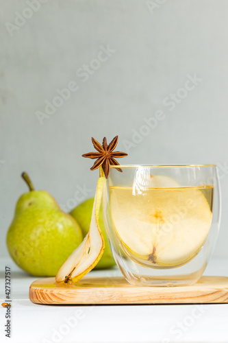 Canvas-taulu A glass of cider, decorated with an anise star and a slice of pear, on a wooden board, fruit in the background