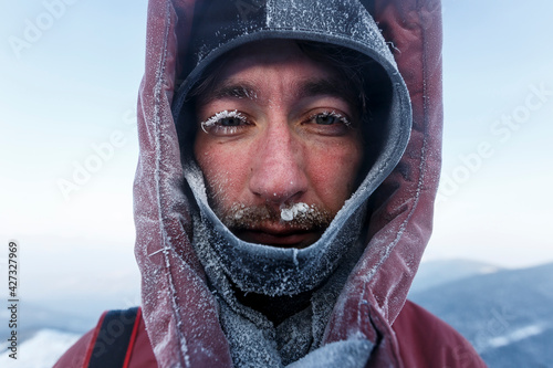 A frozen man in a winter jacket. Close-up. A man's face covered with snow and inium. The traveler looks at the camera.