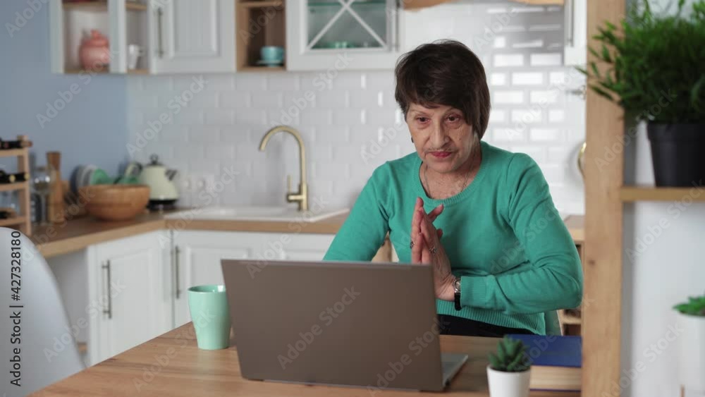 Happy old senior woman communicates by video call using laptop. Grandmother enjoys talking to her grandchildren online. Virtual family conversation at a distance. Remote communication concept. Happy old senior woman communicates by video call using laptop. Grandmother enjoys talking to her grandchildren online. Virtual family conversation at a distance. Remote communication concept.