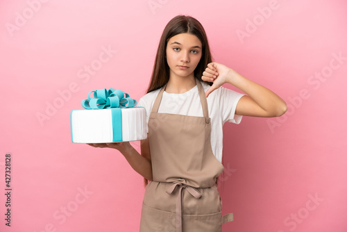 Little girl with a big cake over isolated pink background showing thumb down with negative expression