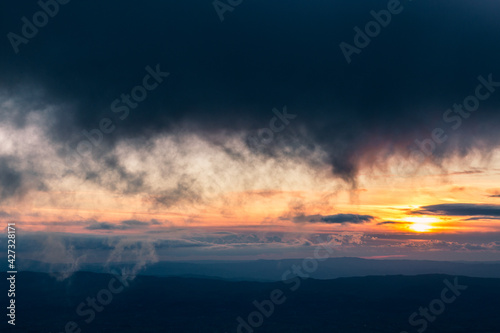 Sunset with sun hidden behind clouds over mountains and valley, with very low and close clouds