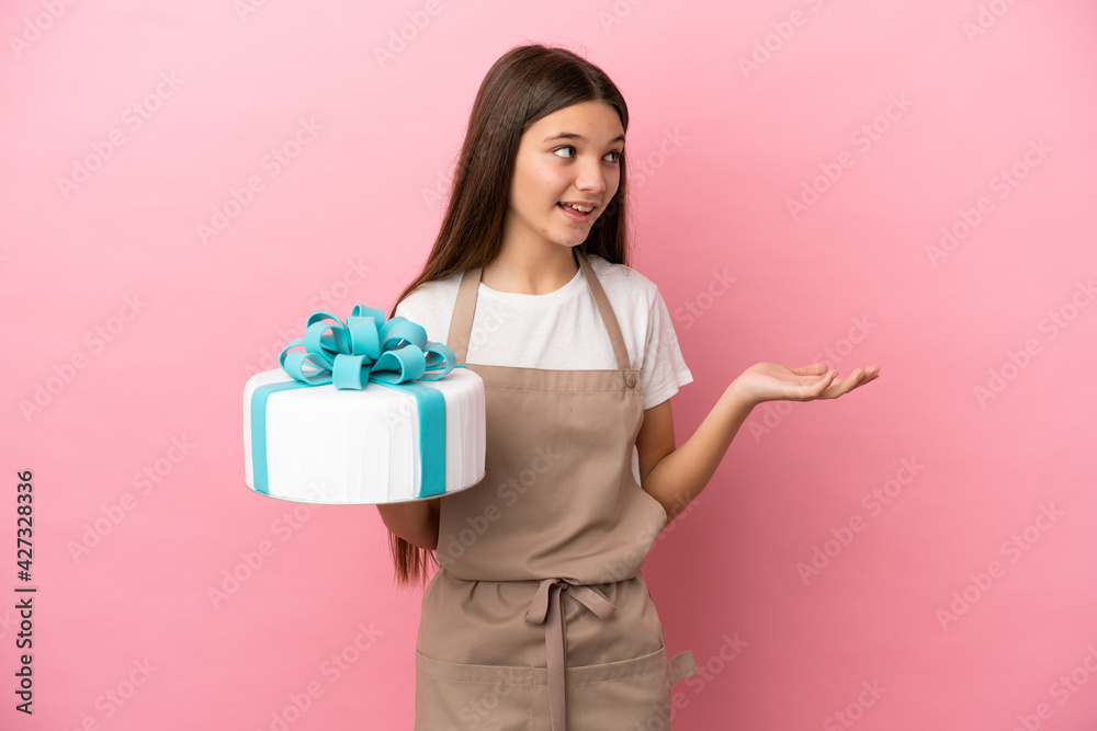 Little girl with a big cake over isolated pink background with surprise expression while looking side Little girl with a big cake over isolated pink background with surprise expression while looking side