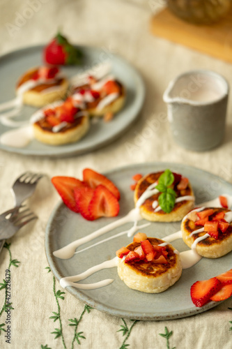 Cottage cheese cakes with strawberries and sour cream on plates