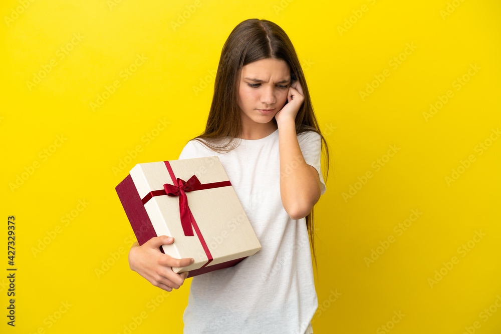 Little girl holding a gift over isolated yellow background frustrated and covering ears Little girl holding a gift over isolated yellow background frustrated and covering ears