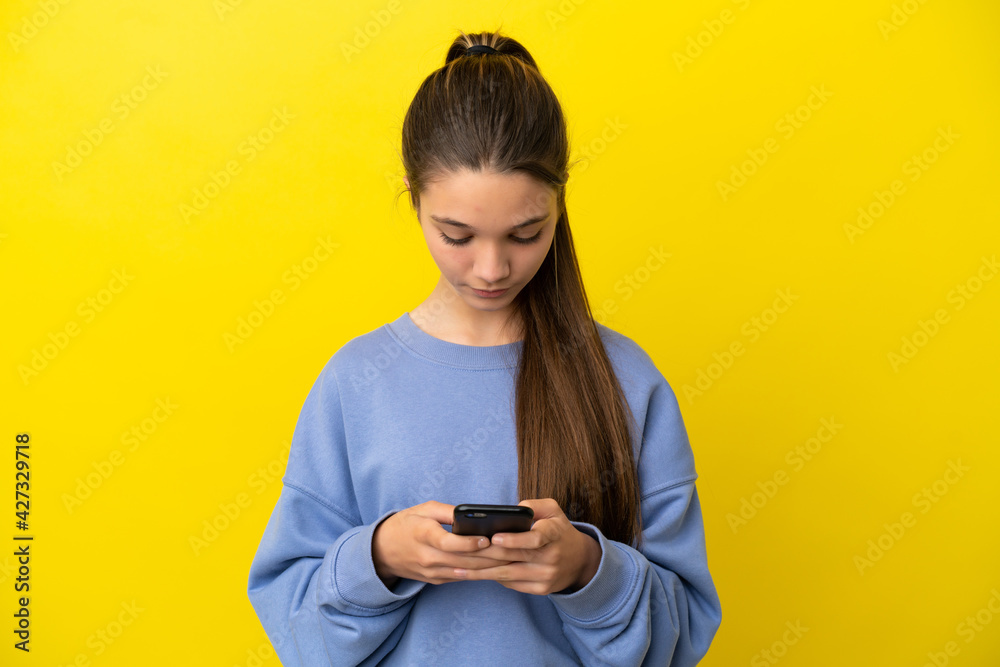 Little girl over isolated yellow background using mobile phone