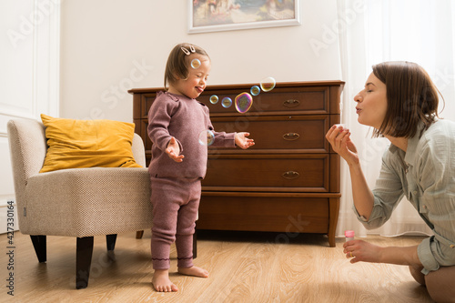 Girl with down syndrome feeling fun while her young mother blowing soap bubbles photo