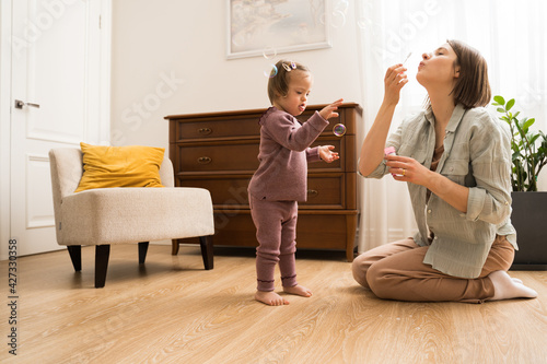 Girl with down syndrome looking while her young mother blowing soap bubbles