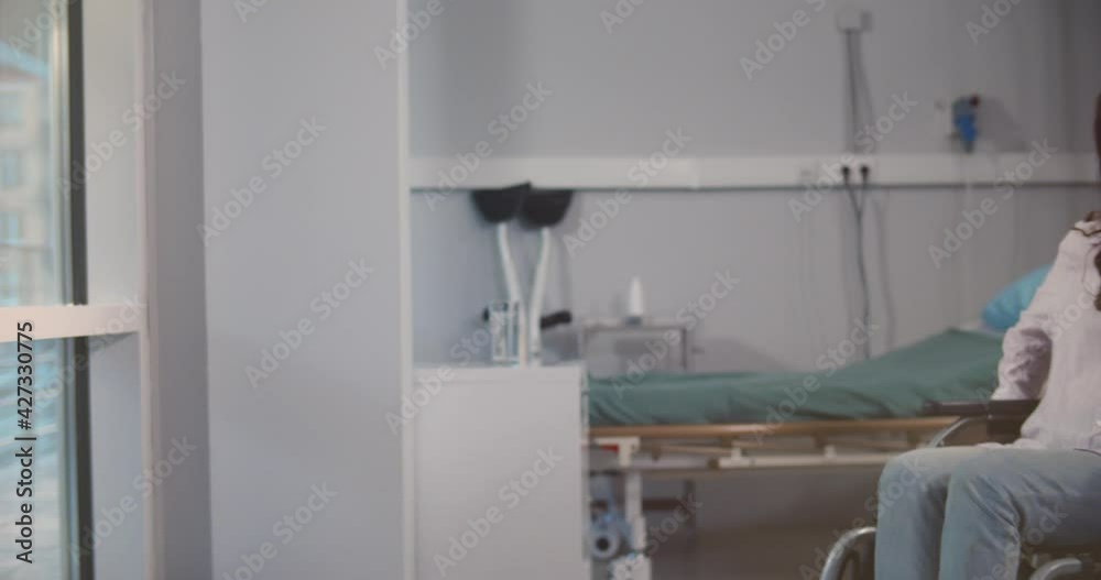 Smiling female patient sitting in wheelchair in hospital room looking through window Smiling female patient sitting in wheelchair in hospital room looking through window