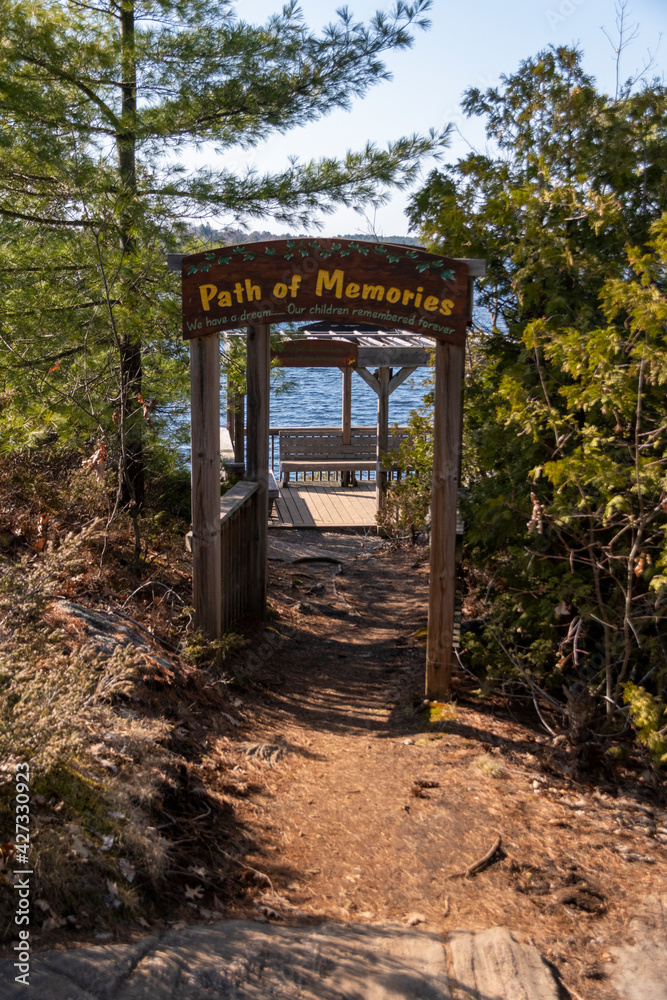 A sign reading Path of Memories leads onto a dock overlooking a lake at the end of a short hiking trail in the small cottage town of Gravenhurst in the Muskoka region of Ontario.