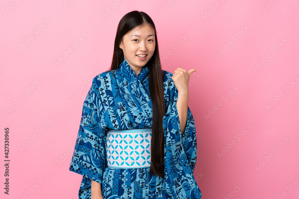 Young Chinese girl wearing kimono over isolated background pointing to the side to present a product Young Chinese girl wearing kimono over isolated background pointing to the side to present a product