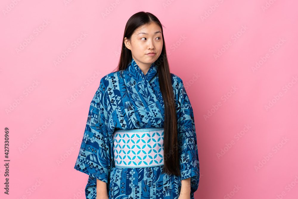 Young Chinese girl wearing kimono over isolated background making doubts gesture looking side