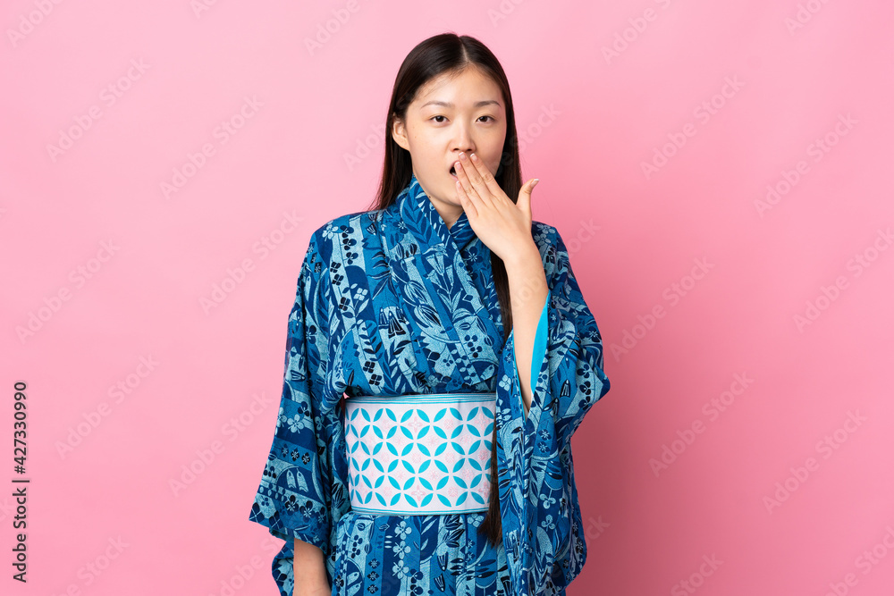 Young Chinese girl wearing kimono over isolated background yawning and covering wide open mouth with hand Young Chinese girl wearing kimono over isolated background yawning and covering wide open mouth with hand