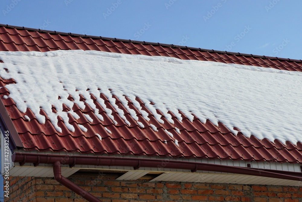 Fototapeta premium part of a private house from a red tile roof under white snow against a blue sky
