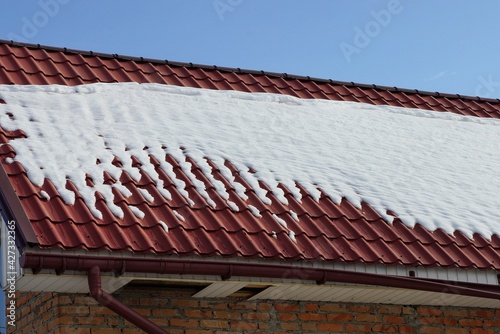 part of a private house from a red tile roof under white snow against a blue sky